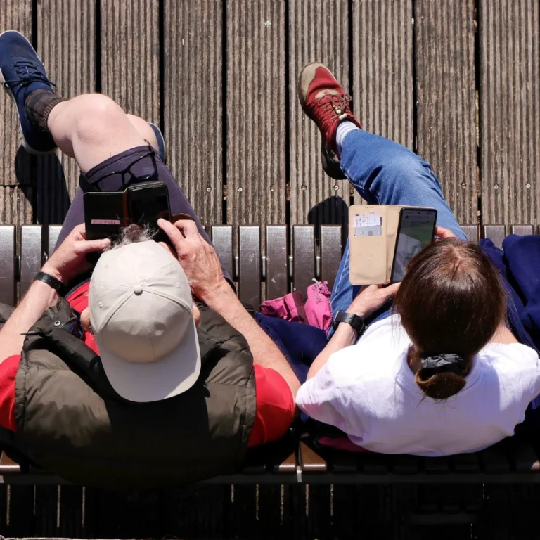 un couple sur un banc en train de chacun regarder son portable