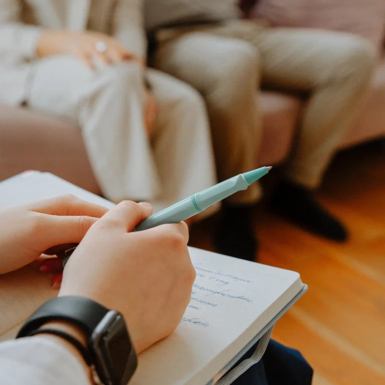 Une main de conseillère conjugale tenant un stylo et un carnet de notes, lors d'une session d'accompagnement en conseil conjugal